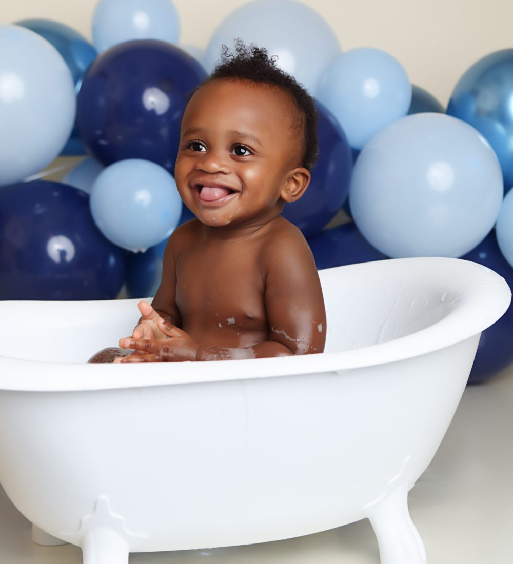 Boston Cake smash portrait of little boy taking a buble bath. Blue balloon garland in background.