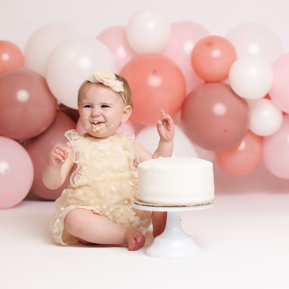 Boston Cake Smash session of one year old little girl with pink theme smiling while eating cake.