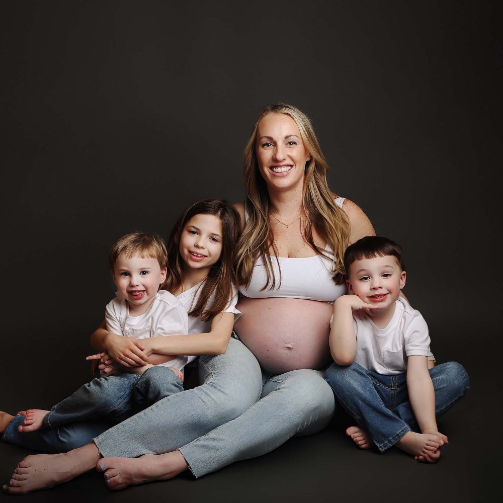 Maternity portrait of mother wearing a tank top and jeans while posing with her children.