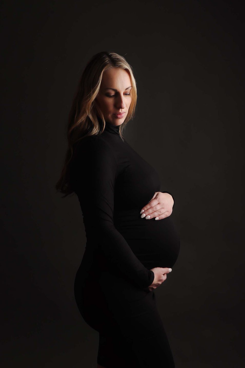 Boston Maternity Portrait Session of expectant mother all in black posing with one light on dark backdrop.