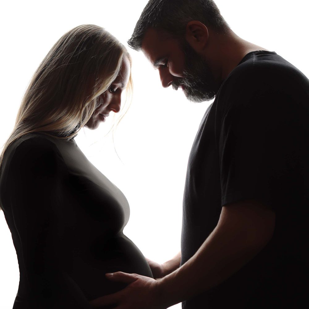 Boston Maternity Portrait of mother-to-be posing with husband. Backlit image.