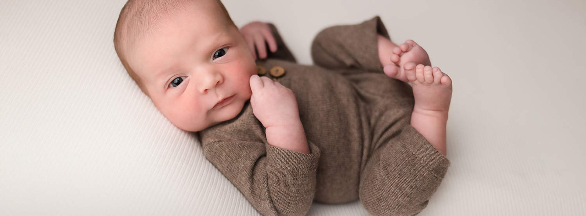 NH Newborn Portrait - Baby Boy in knit brown romper looking at the camera.