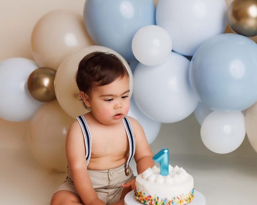 One year old looking at birthday cake for a cake smash portrait.