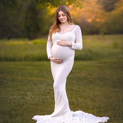 Maternity portrait of expectant mother in ivory fitted gown posing in open field.