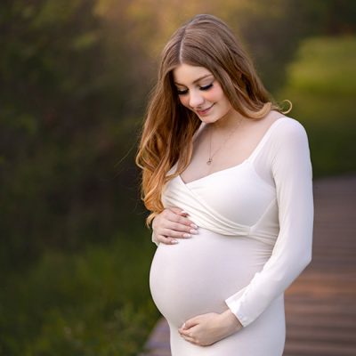 Maternity portrait of expectant mother in ivory gown looking down at her stomach.